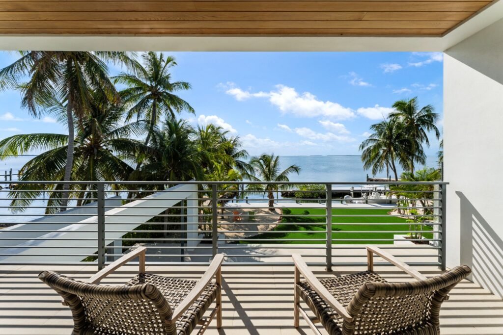 Second-story balcony terrace at 19 Avacado Street in Islamorada, featuring wicker lounge chairs, modern metal railings, and panoramic sunset-facing bay views.