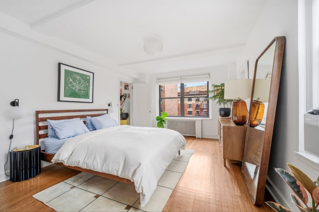 Sun-filled pre-war bedroom with hardwood floors, a large floor mirror, and open city views at 140 East 28th Street in Manhattan, New York.