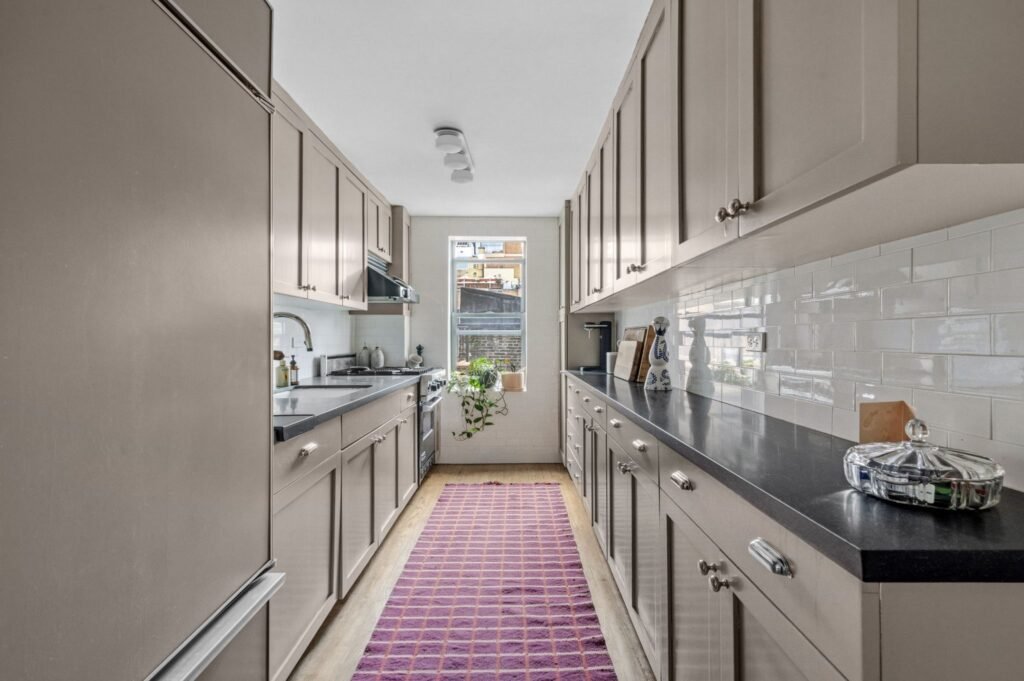 Updated galley kitchen with modern appliances, grey cabinets, black countertops, and a white subway tile backsplash at 140 East 28th Street in Manhattan, New York.