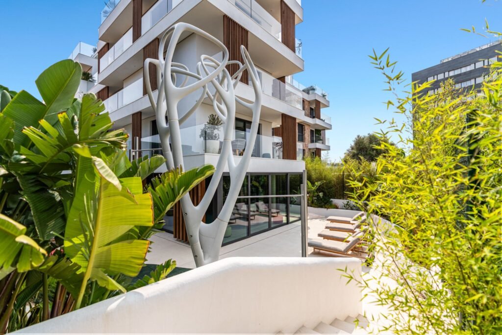 Vibrant new build apartment exterior in Playa d’en Bossa, Ibiza, featuring modern architecture, tropical landscaping, and a sunny pool terrace.