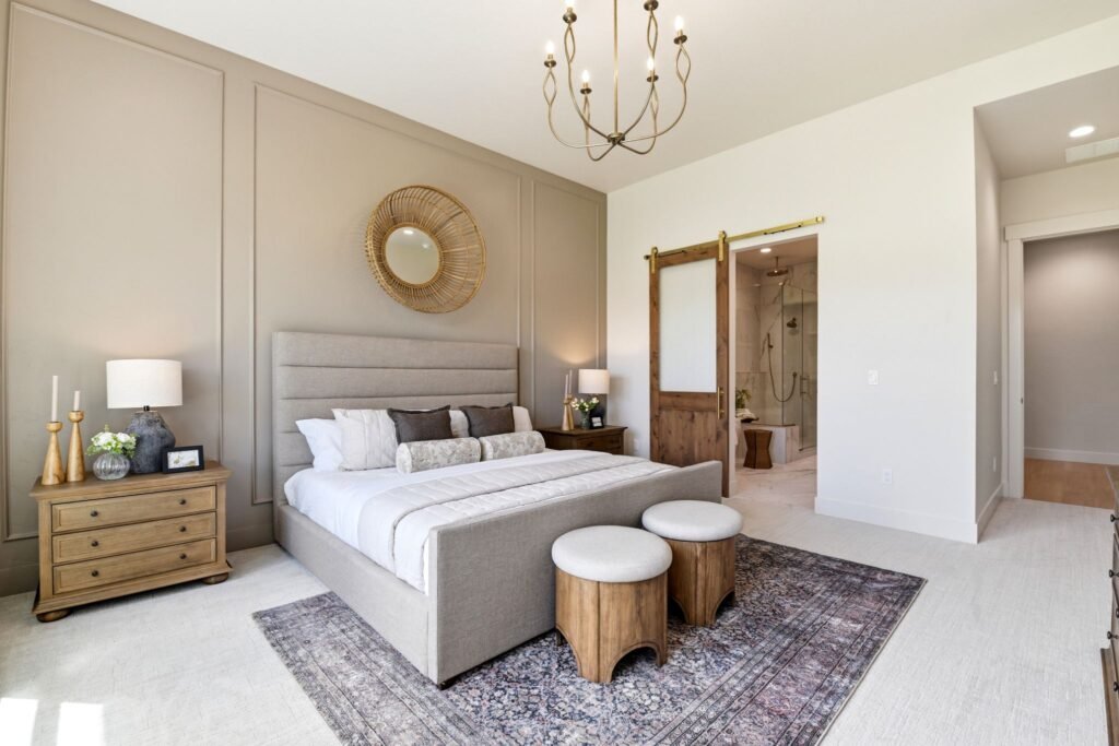 Award-winning Spanish Mission primary bedroom at 7042 E Chicken Hawk Loop in Nampa, Idaho, featuring a warm beige accent wall, wooden barn door, and ensuite bathroom view.