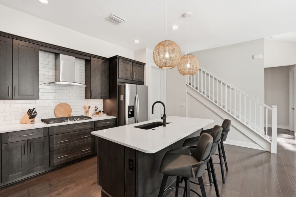 Modern open-concept kitchen featuring dark wood cabinets, a white quartz island with seating, a white subway tile backsplash, and a staircase view at 9194 Cayman Drive in Naples, Florida.