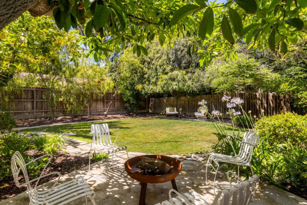 Fenced-in backyard with green lawn, a stone patio fire pit area, and mature fruit trees at 22051 Celes Street in Woodland Hills, California.