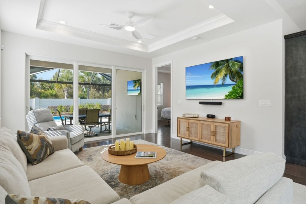 Bright open-concept living room with a tray ceiling and sliding glass doors opening to a screened lanai at 9194 Cayman Drive in Naples, Florida.