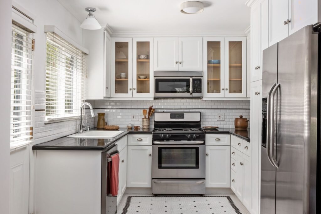 Updated white U-shaped kitchen featuring stainless steel appliances, dark countertops, a white subway tile backsplash, and tile flooring at 22051 Celes Street in Woodland Hills, California.