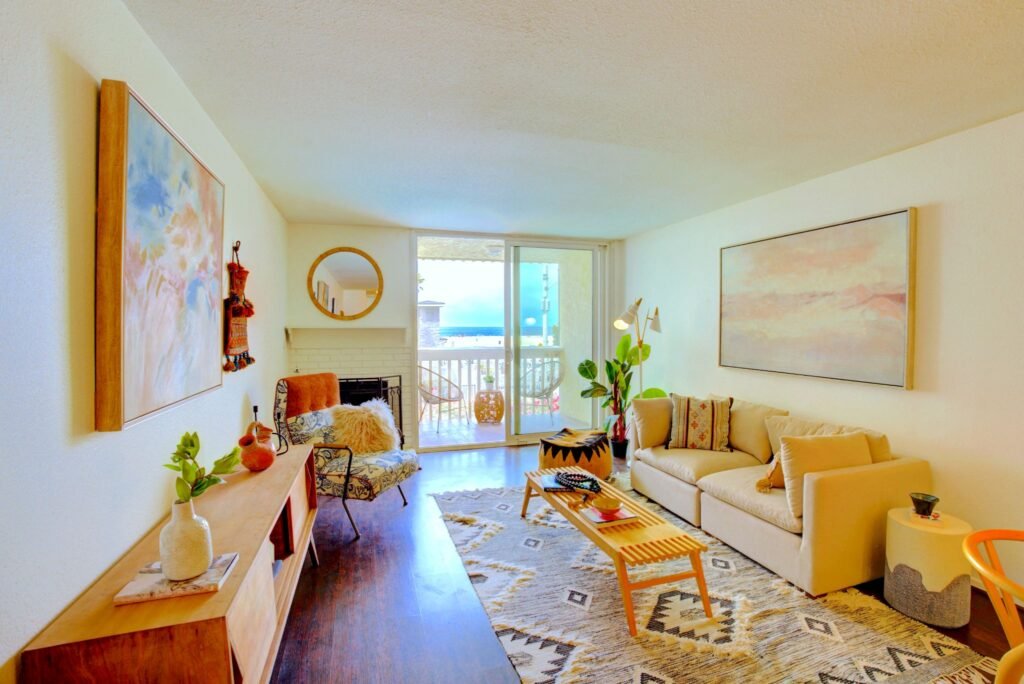 Bohemian open-concept apartment living room with a brick fireplace and a sliding glass door leading to a patio with beach views at 22 Navy Street in Venice, California.