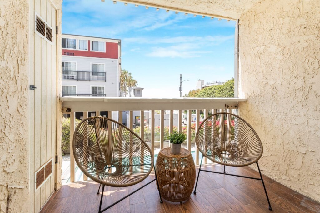 Breezy covered patio at 22 Navy Street in Venice, California, featuring woven acorn chairs, wood-look flooring, and a view overlooking the community heated pool and spa.