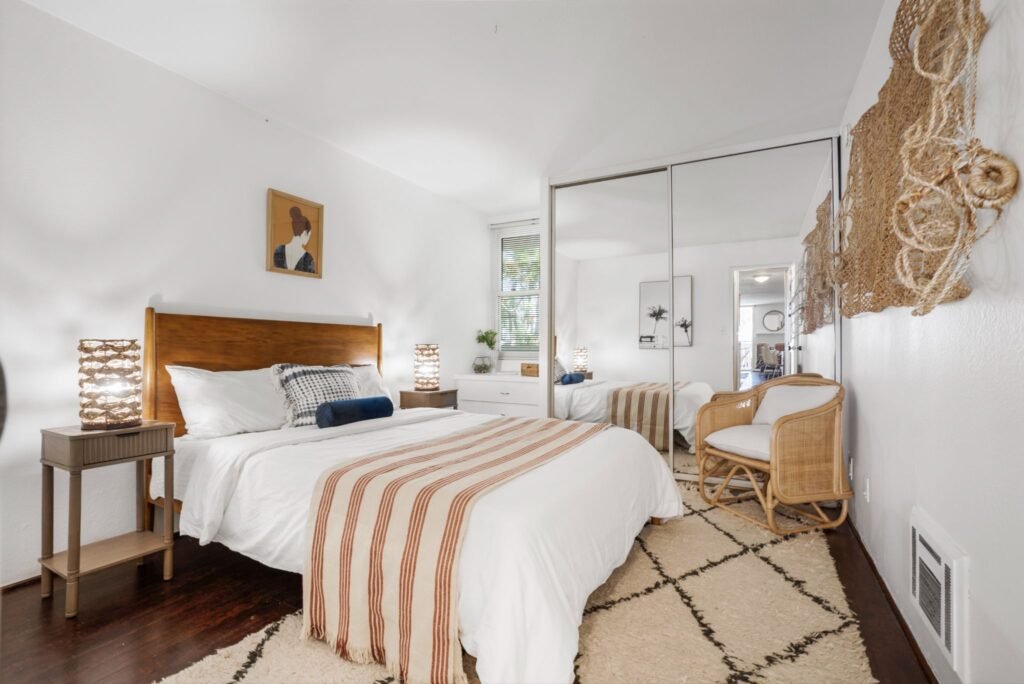 Bohemian style bedroom with dark hardwood floors, large mirrored closet doors, and woven decor accents at 22 Navy Street in Venice, California.