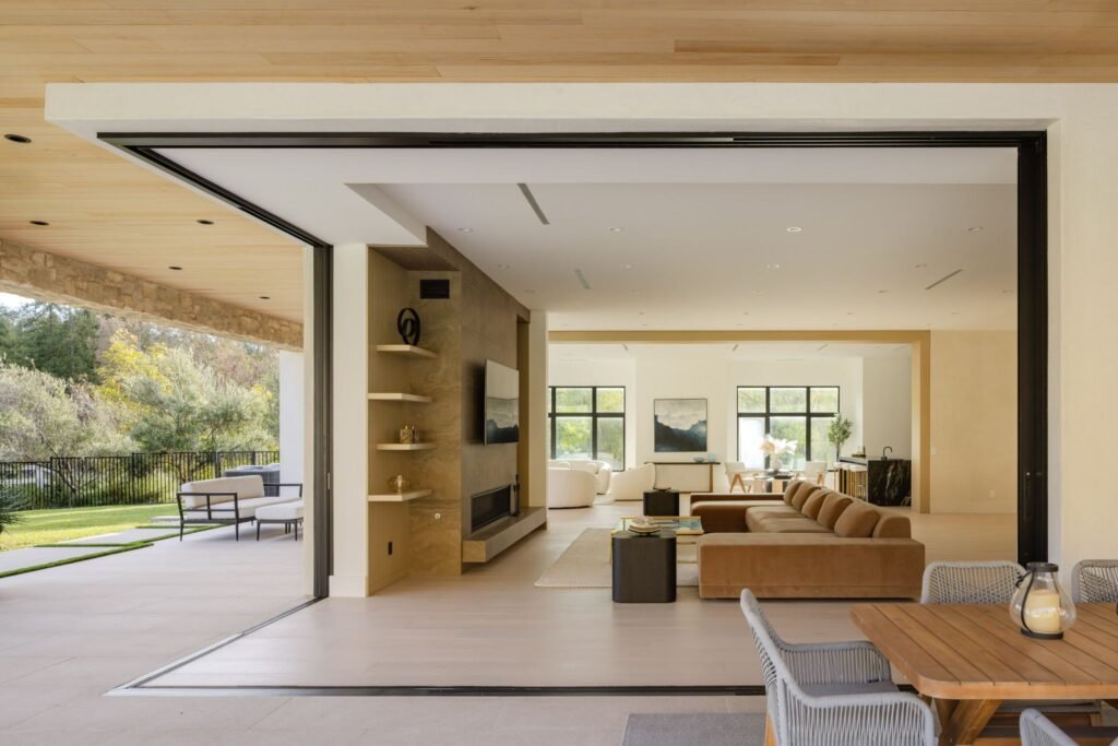 Modern open-concept living room with large pocket sliding glass doors transitioning to a covered patio with outdoor dining furniture.