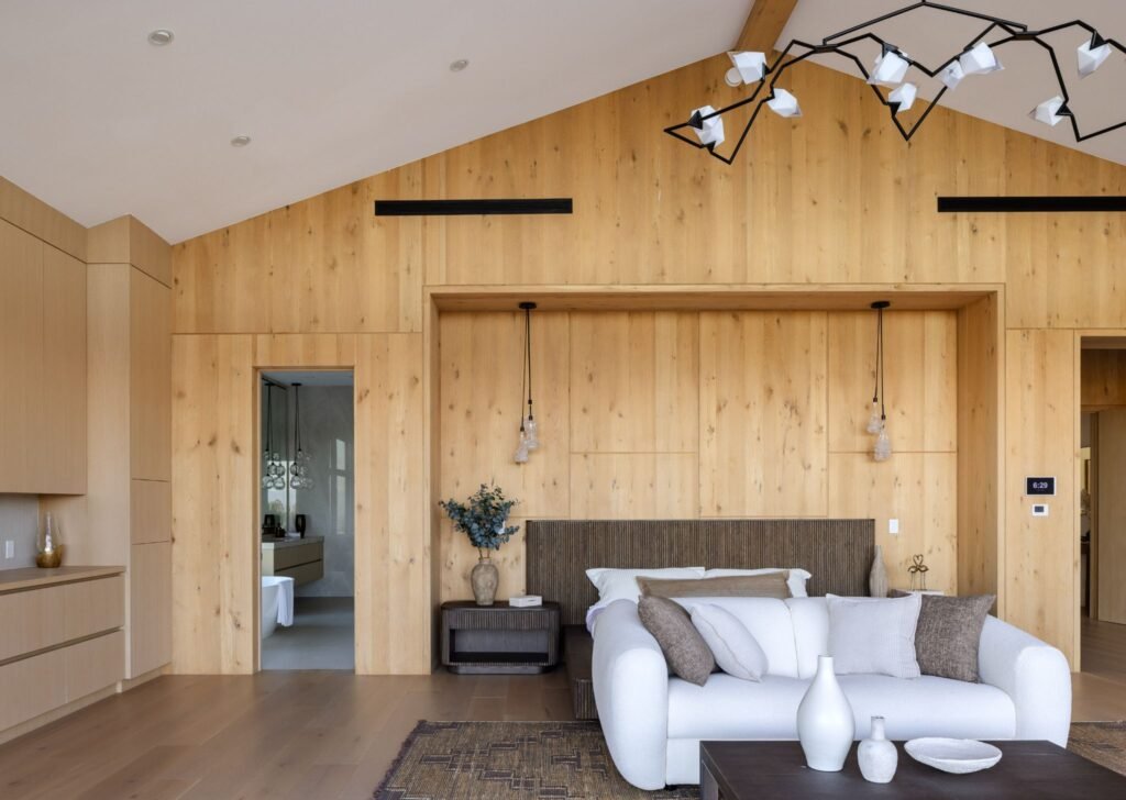 Modern luxury bedroom suite featuring a white sofa, custom integrated wood panel headboard recess, and an architectural geometric branch chandelier.