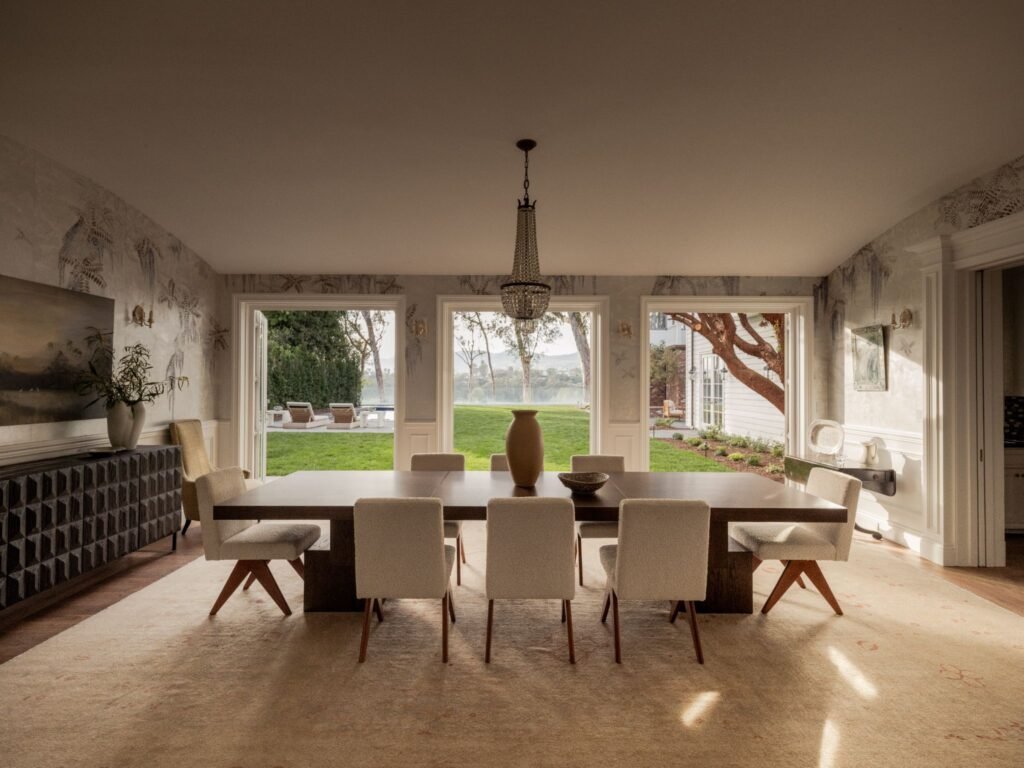 Upscale dining area in an estate home showcasing panoramic backyard views, elegant wainscoting, a designer rug, and seamless indoor-outdoor flow.