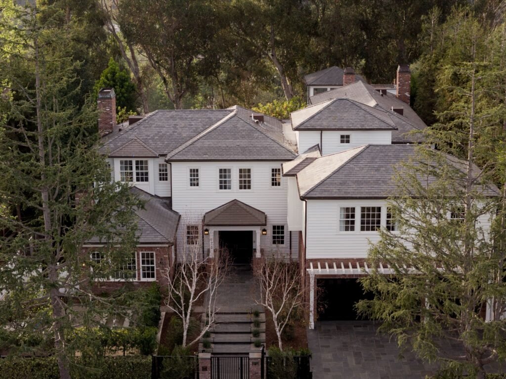 Grand exterior facade of a luxury estate showcasing traditional architecture, multiple custom chimneys, premium landscaping, a gated entryway, and a private wooded setting.