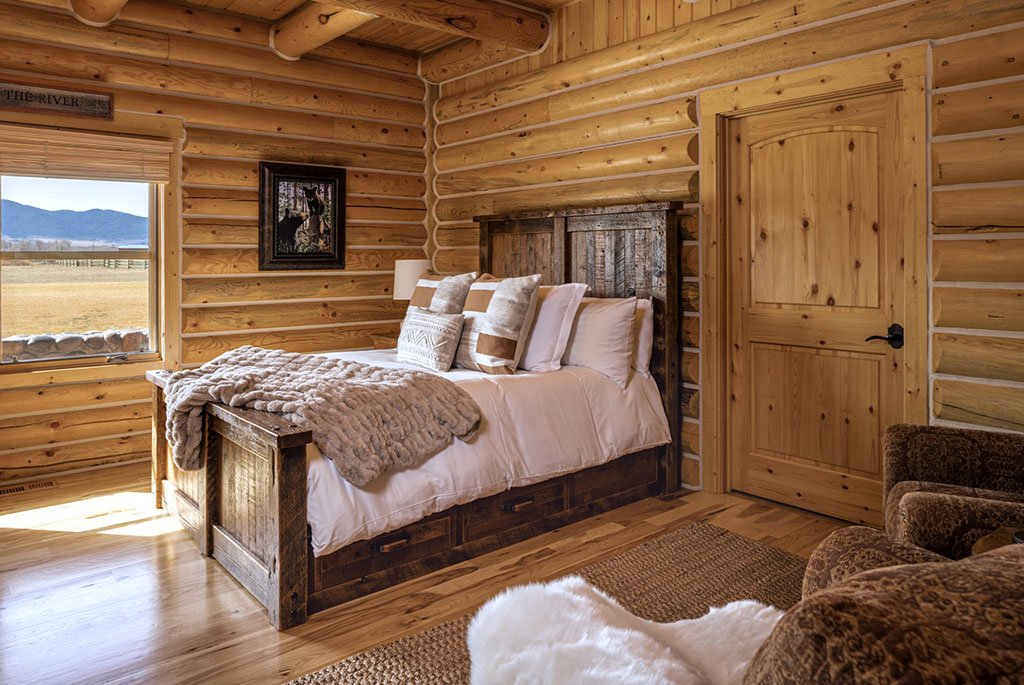 The expansive back bedroom at A River's Ranch featuring a self-contained guest suite layout with hand-hewn logs, a sitting area, and pasture views.