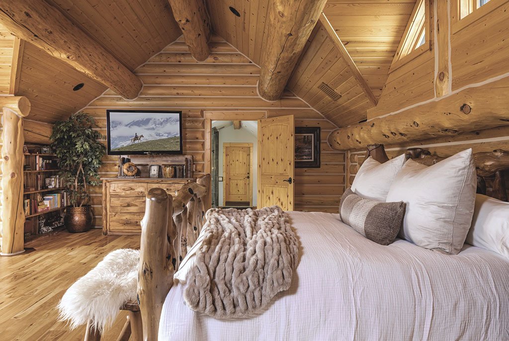 Custom primary suite at A River's Ranch featuring golden hand-hewn logs, vaulted ceilings, a rustic wooden bed frame, and a wall-mounted TV.