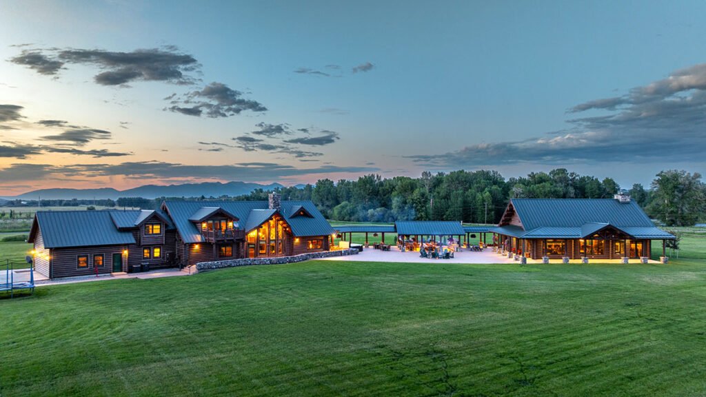 An aerial dusk view of the main estate, guest house, and covered outdoor kitchen pavilions at A River's Ranch under a twilight Montana sky.