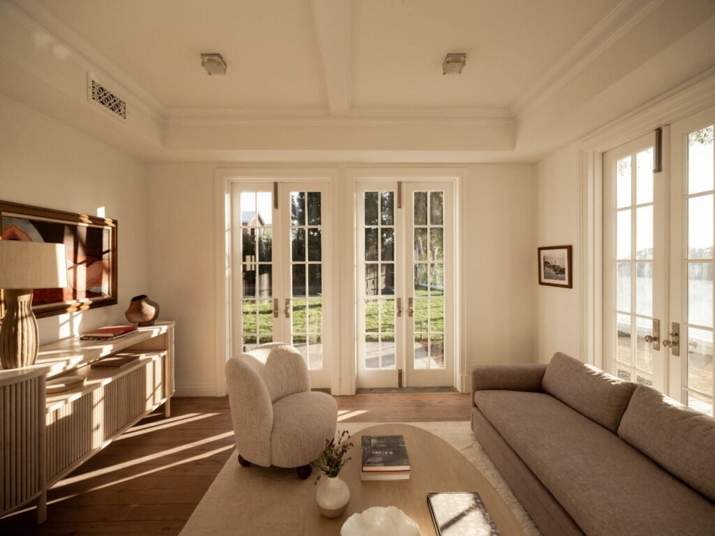 Bright sunlit family room in an estate home showcasing wide-plank hardwood floors, elegant tray ceilings, custom millwork, and seamless indoor-outdoor transition.