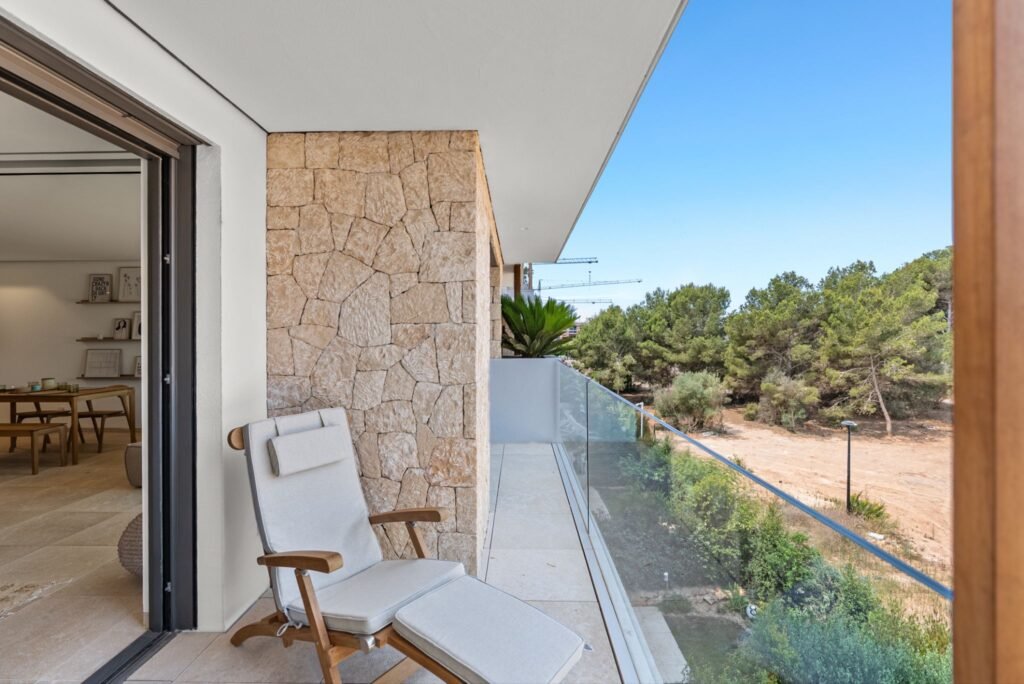 Spacious terrace lounge of a Playa d’en Bossa, Ibiza apartment overlooking a planned park area with stone accents and glass railings.
