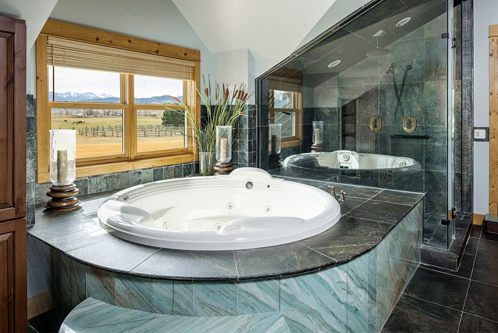 Primary suite bathroom at A River's Ranch featuring jade-colored quartz, a large soaking tub, a glass shower, and a window overlooking horse pastures.