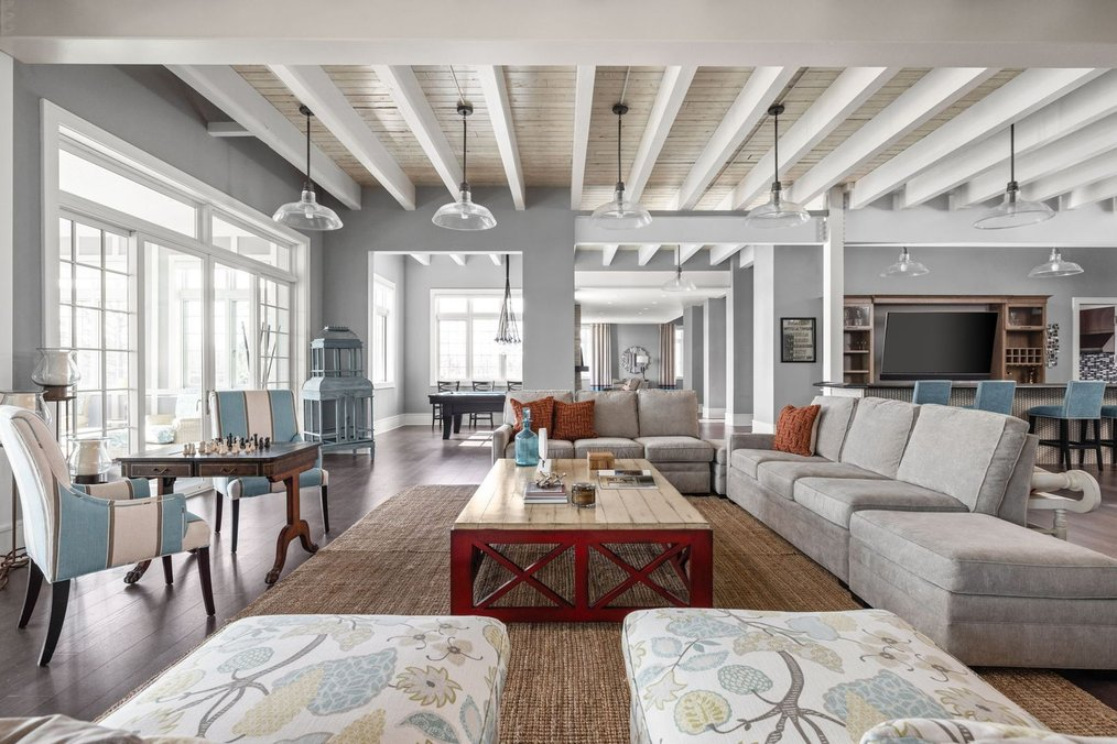 An open-concept luxury basement living room and entertainment space at 9825 Windy Hills Drive in Zionsville, Indiana, featuring white ceiling beams, large sectional sofas, a game table, and a clear view of a bar and pool table in the background.