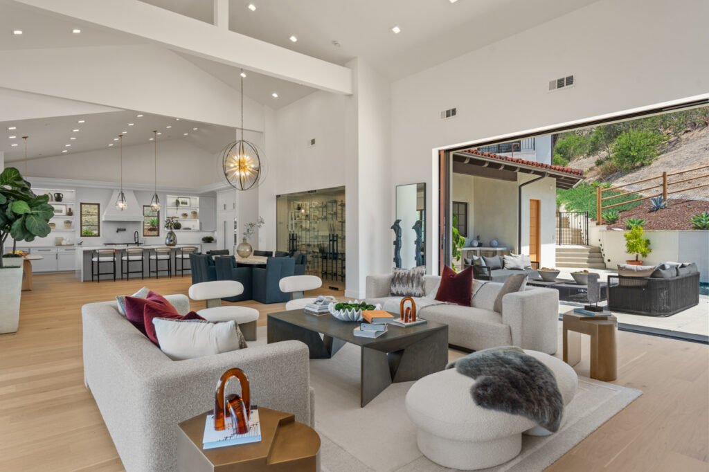 The open-concept main living space at 5758 Las Palomas in Rancho Santa Fe, California, featuring high vaulted ceilings, modern furniture, a clear view into the kitchen, and a massive pocket glass wall opening completely to an outdoor patio.