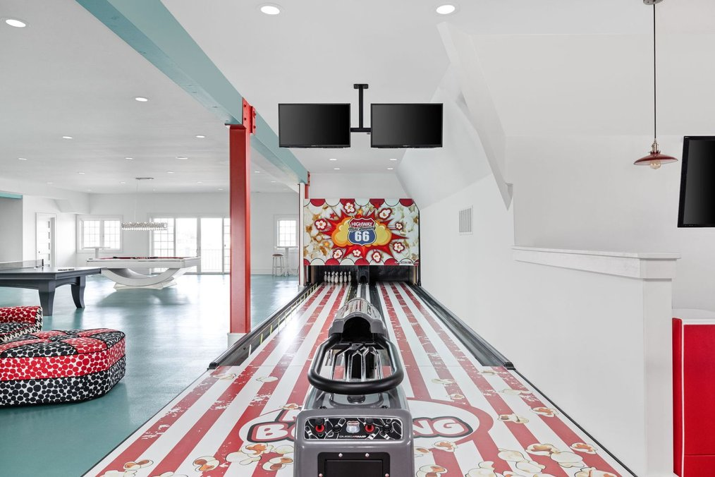 A private two-lane bowling alley inside the basement entertainment center at 9825 Windy Hills Drive in Zionsville, Indiana, featuring a retro Highway 66 theme, digital score screens, popcorn-patterned lanes, and a nearby billiards area.