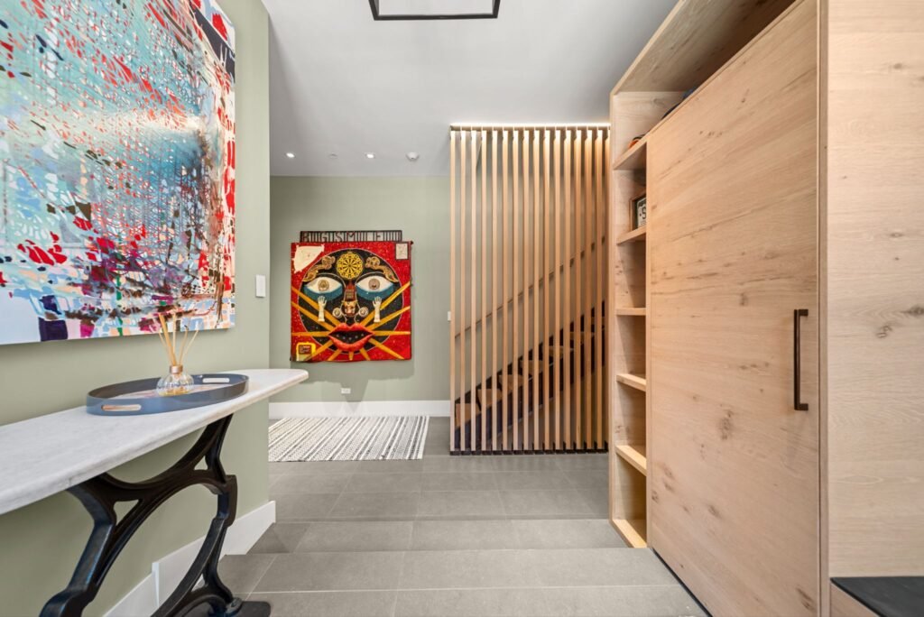 Modern luxury entryway at 150 W Pacific Avenue in Telluride, featuring grey tile flooring, large contemporary art pieces, a wooden slat privacy screen by the stairs, and custom light oak cabinetry.