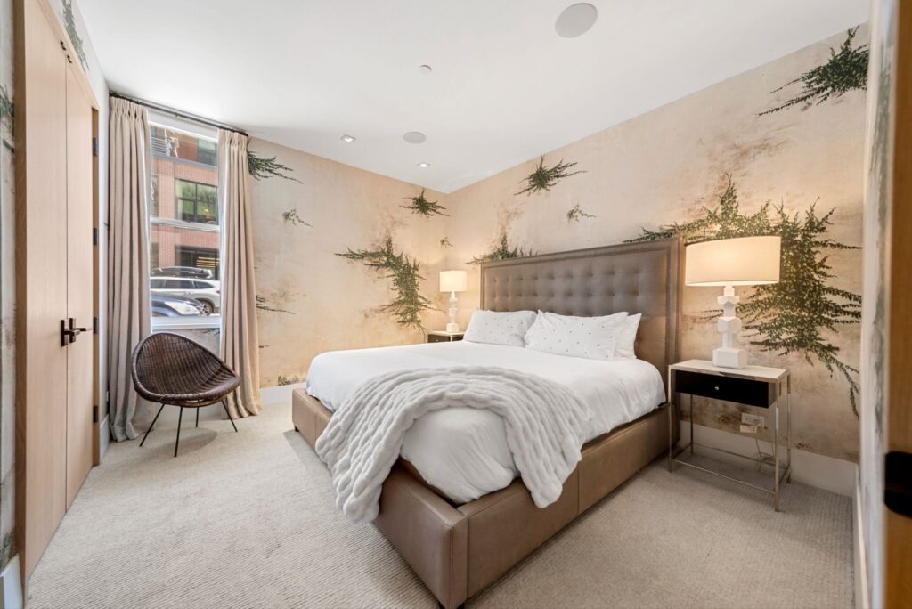 Luxury guest bedroom at 150 W Pacific Avenue in Telluride, featuring custom watercolor floral wallpaper, a tufted leather headboard, a white chunky knit blanket, and modern geometric bedside lamps.