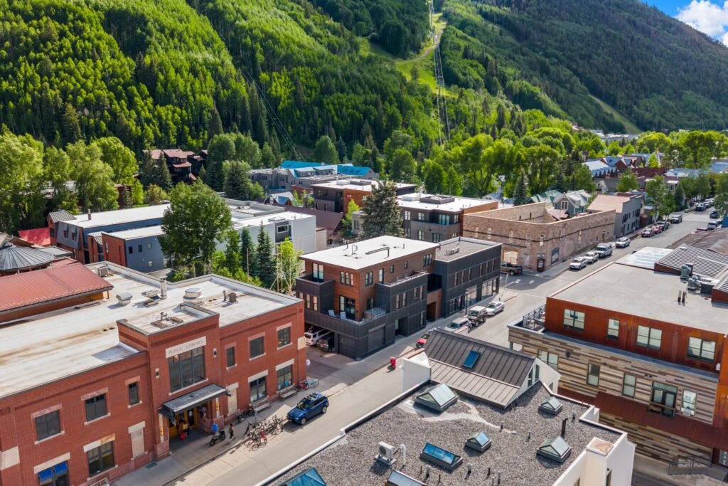 Aerial view of downtown Telluride, Colorado, featuring the modern Arthouse building complex at 150 W Pacific Avenue set against the lush green pine trees and ski slopes of the Rocky Mountains.