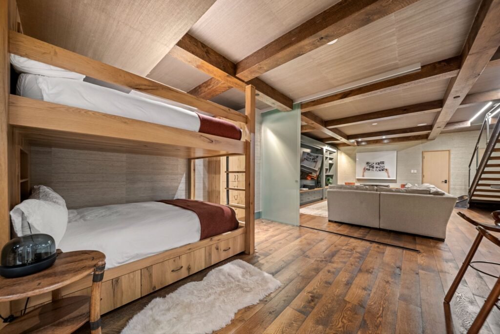 Luxury lower-level bunk room at 150 W Pacific Avenue in Telluride, featuring custom built-in wooden bunk beds, hardwood floors, exposed ceiling beams, and a retractable frosted glass divider door opening to the media lounge.