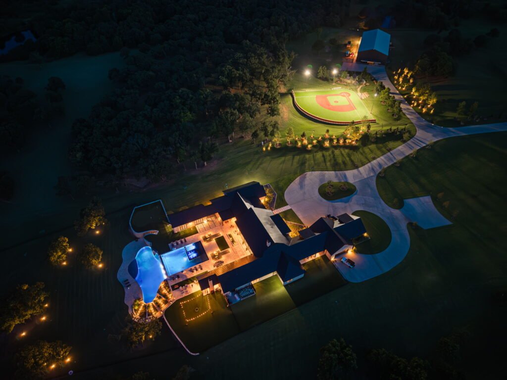 Night aerial view of the illuminated luxury compound and sports field at 3003 Country Club Drive in Stillwater Oklahoma.