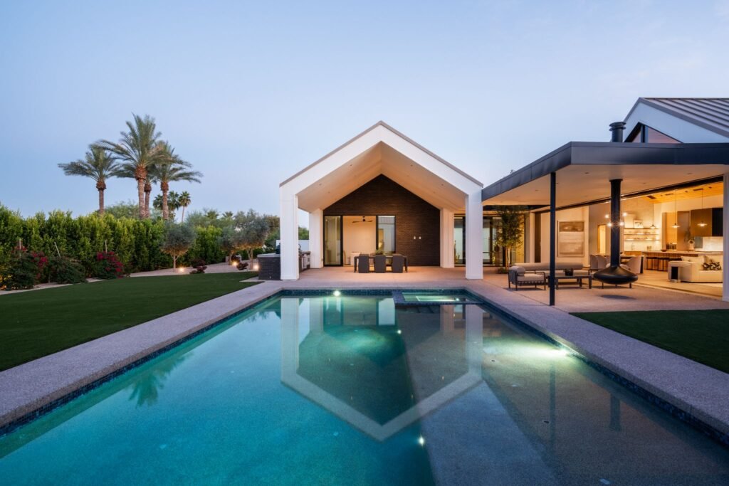 Modern Paradise Valley luxury home designed by The Ranch Mine, highlighting a resort-style swimming pool, an outdoor dining pavilion, a hanging fireplace, and an expansive covered patio layout.