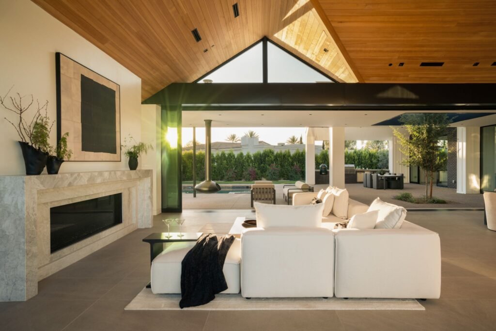 Modern indoor-outdoor living room architecture by The Ranch Mine in Paradise Valley, AZ, showcasing a vaulted wood paneled ceiling, a sleek modern fireplace, and large sliding pocket doors that reveal a luxury backyard patio