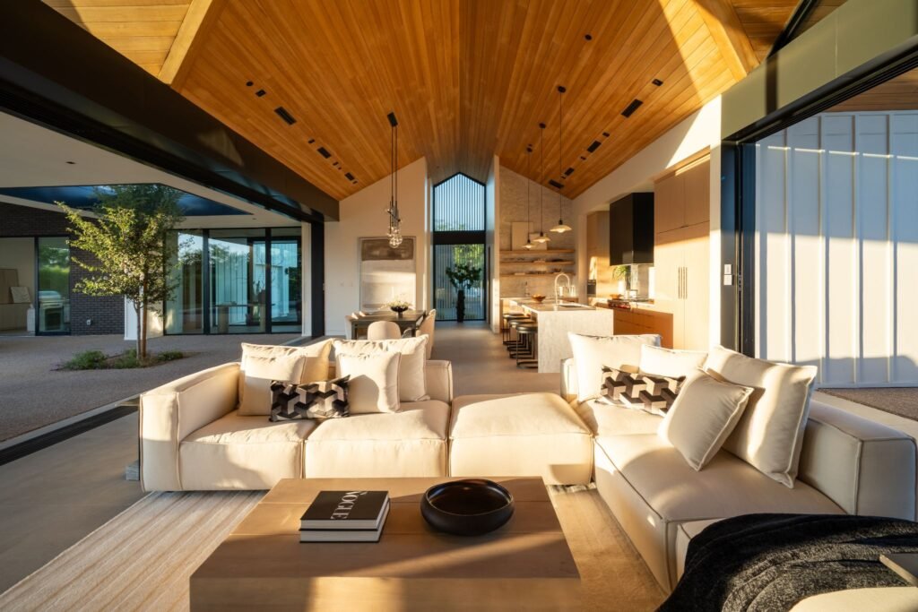 Modern great room architecture by The Ranch Mine in Paradise Valley, AZ, showcasing a seamless indoor-outdoor floor plan with a vaulted wood ceiling, custom kitchen cabinetry, and large sliding doors opening to a central courtyard.