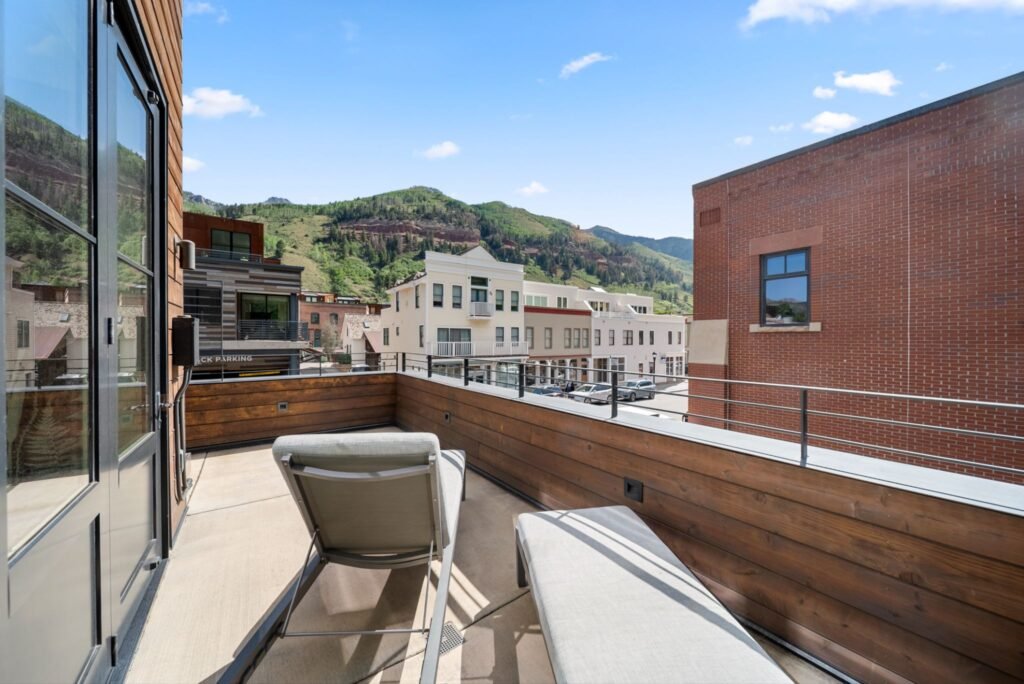Luxury outdoor patio at 150 W Pacific Avenue in Telluride, featuring a wood-paneled balcony with comfortable lounge chairs, glass double doors, and scenic views of the surrounding Rocky Mountain valley.