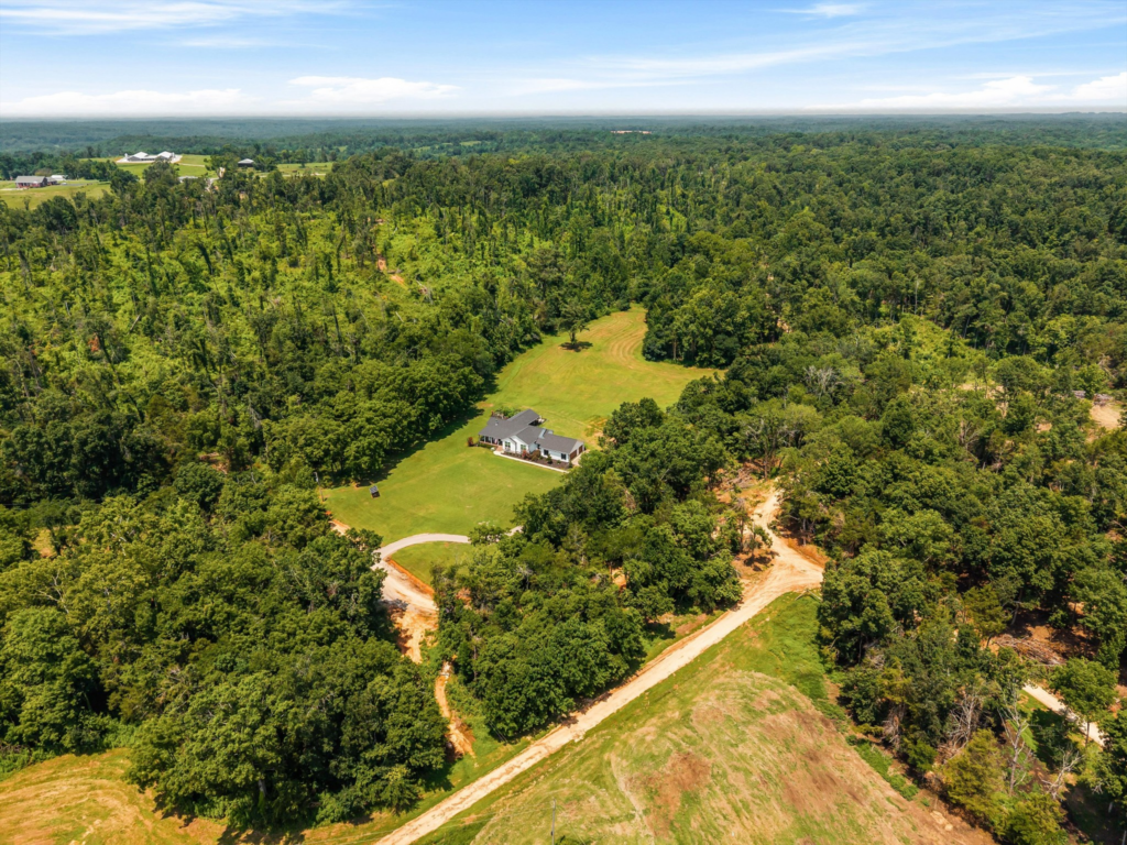 An aerial view of the 144-acre multi-generational family compound and organic farm at 121 Harbor Lane in Hickory Creek, Texas, featuring a private luxury residence surrounded by expansive green meadows, dense mature timber forest, and open space.