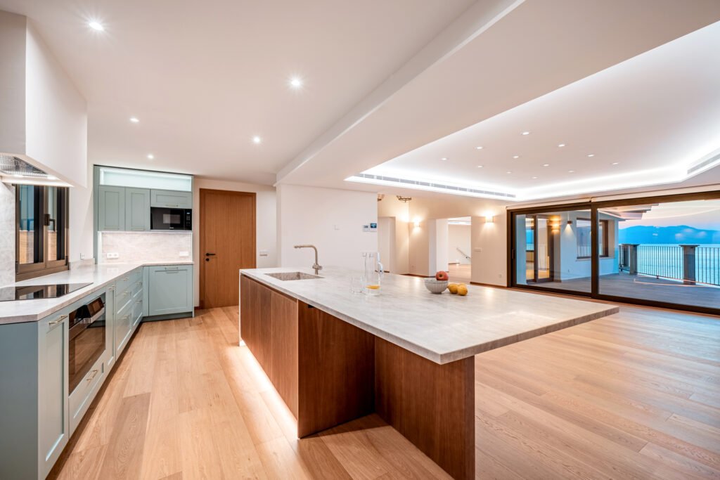 Modern open-plan kitchen with marble island, mint green cabinets, and large sliding glass doors facing the sea in a Mallorca villa.