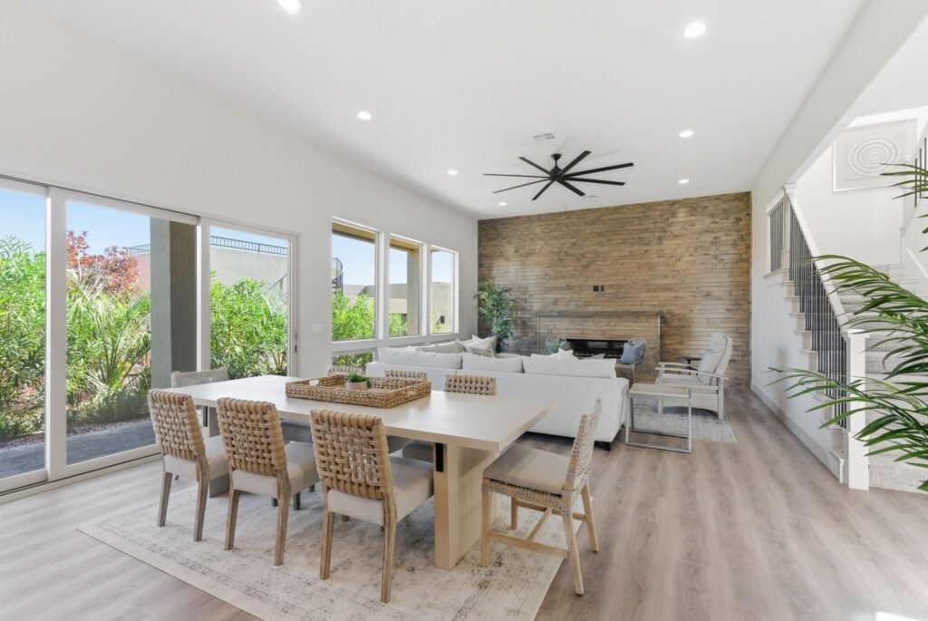 Luxury real estate interior at Tava Resort, Utah, showcasing a large wooden dining table with woven chairs next to a bright, sunlit living area and staircase.