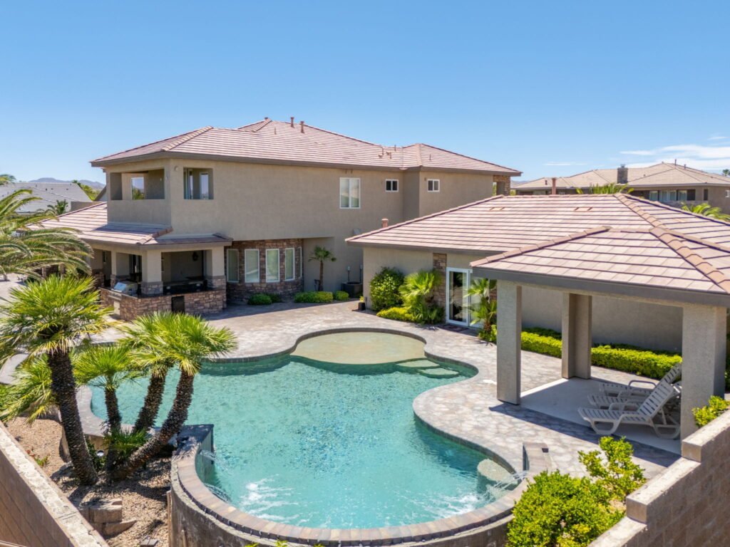Elevated view of a custom multi-generational property at 208 E Levi Avenue in Las Vegas showcasing a freeform swimming pool, integrated spa, stone-paved deck, covered cabana, and outdoor kitchen setup.