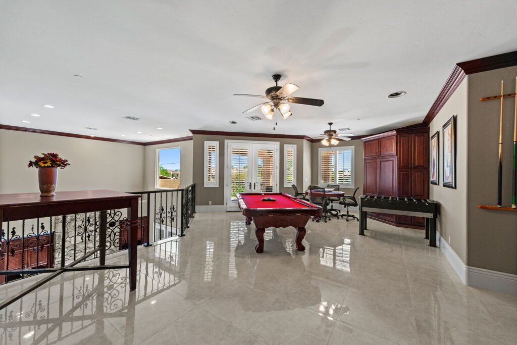 Upper-level entertainment loft inside a custom mansion at 208 E Levi Avenue in Las Vegas showing a red pool table, foosball table, card game seating, polished marble floors, and crown molding.