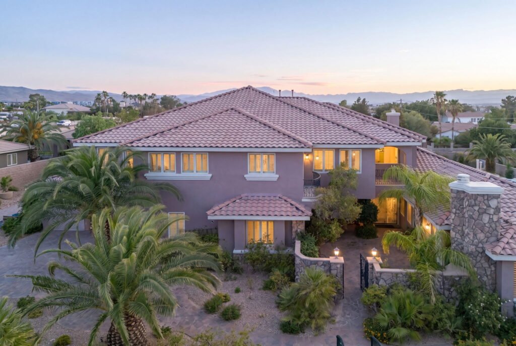 Twilight drone view of a luxury multi-generational residence at 208 E Levi Avenue in Las Vegas showcasing a stone entryway, gated courtyard, paved driveway, and mountain views in the background.