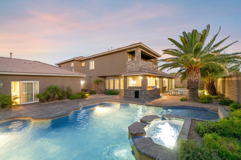 Rear exterior of a multi-story home at 208 E Levi Avenue in Las Vegas highlighting a large illuminated swimming pool, a custom stone spa with a waterfall, a built-in outdoor kitchen grill station, and palm trees.