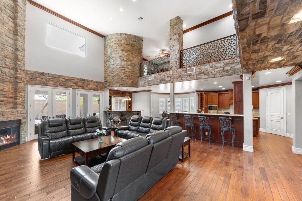 Great room inside a custom residence at 208 E Levi Avenue in Las Vegas showing a stone fireplace, black leather sofas, a built-in bar, wood cabinetry, and an upper-level overlook with custom ironwork.