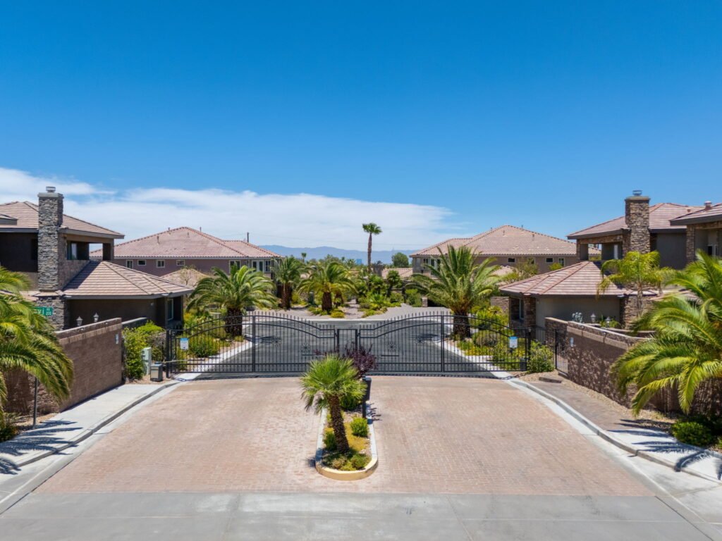 Secure entrance gate at 208 E Levi Avenue in Las Vegas showcasing a brick-paved entry road, wrought-iron security gates, flanking custom homes, and palm tree landscaping.