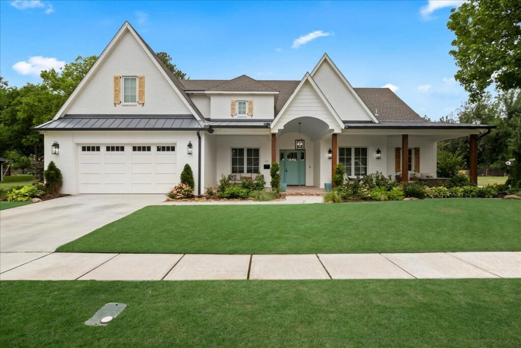 Front exterior view of the record-breaking modern farmhouse estate at 4311 N. Peniel Avenue in Bethany, Oklahoma, featuring a white brick facade, dark metal roofing accents, a light blue front door, a spacious concrete driveway with a garage, and a manicured green front yard.