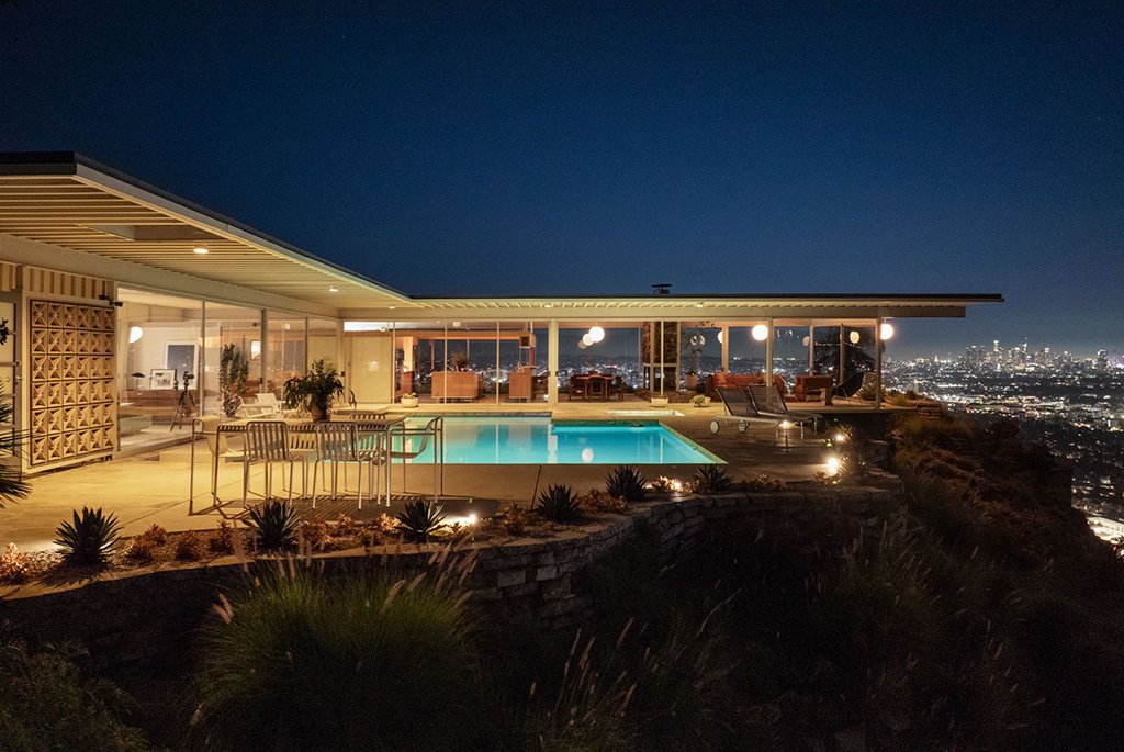 Modern night view of the Stahl House Case Study House 22 showing the illuminated swimming pool, glass pavilion architecture, and expansive Los Angeles skyline lights.