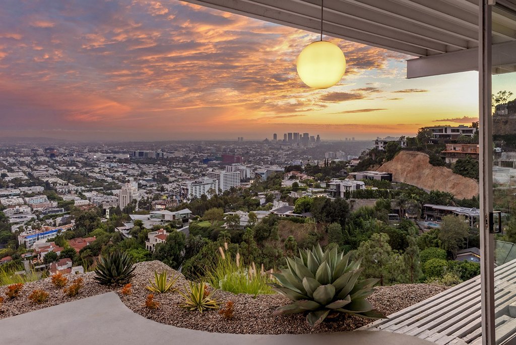 Panoramic sunset view of the Los Angeles skyline from the Stahl House Case Study House 22 featuring a hanging globe pendant light and desert landscaping.