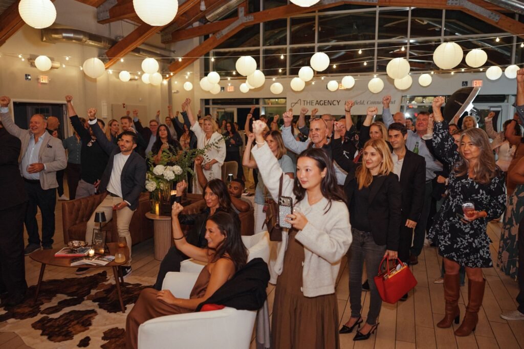 Guests and real estate agents cheering with fists raised on the dance floor during the vibrant launch party for The Agency Fairfield.