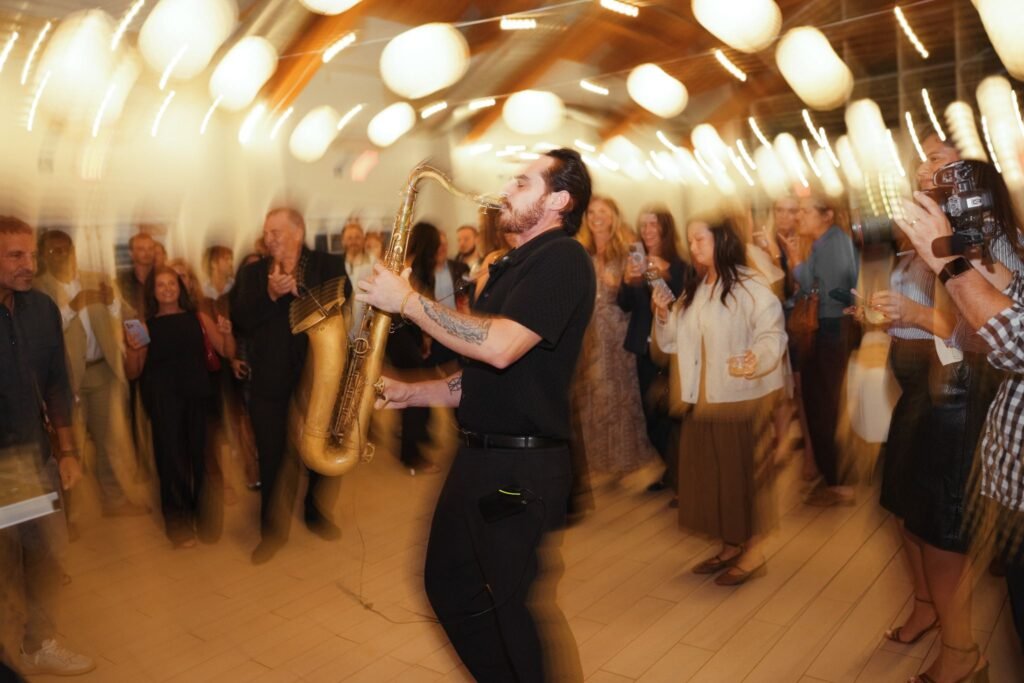 A live saxophone player performing for dancing guests on the dance floor during the high-energy launch party for The Agency Fairfield.