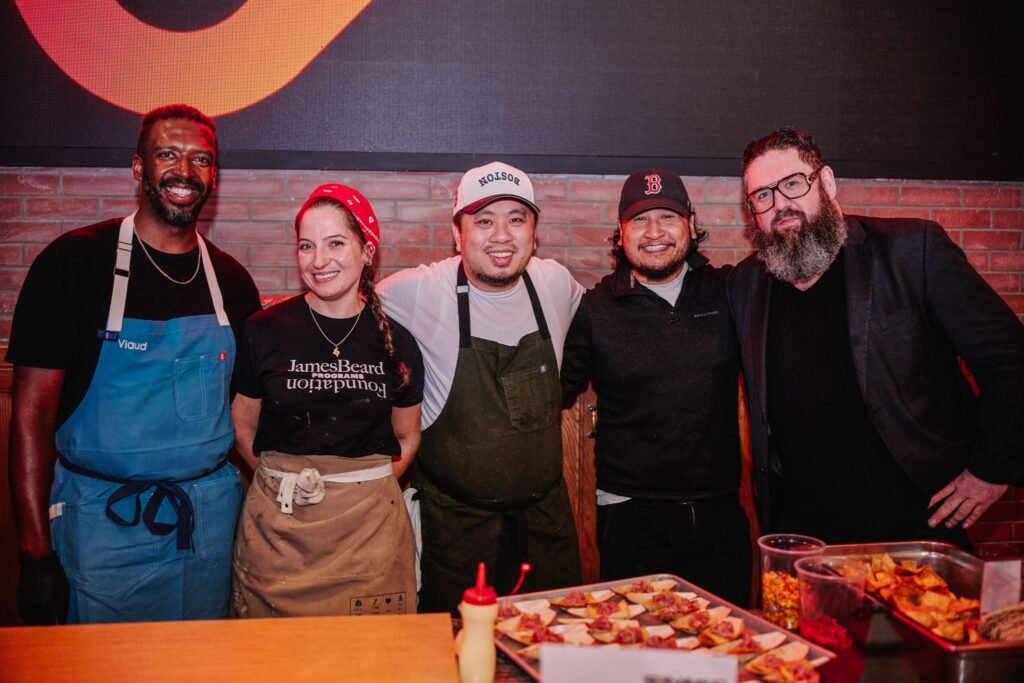 A group of professional chefs and catering staff posing behind a food station at a corporate networking reception in Boston.