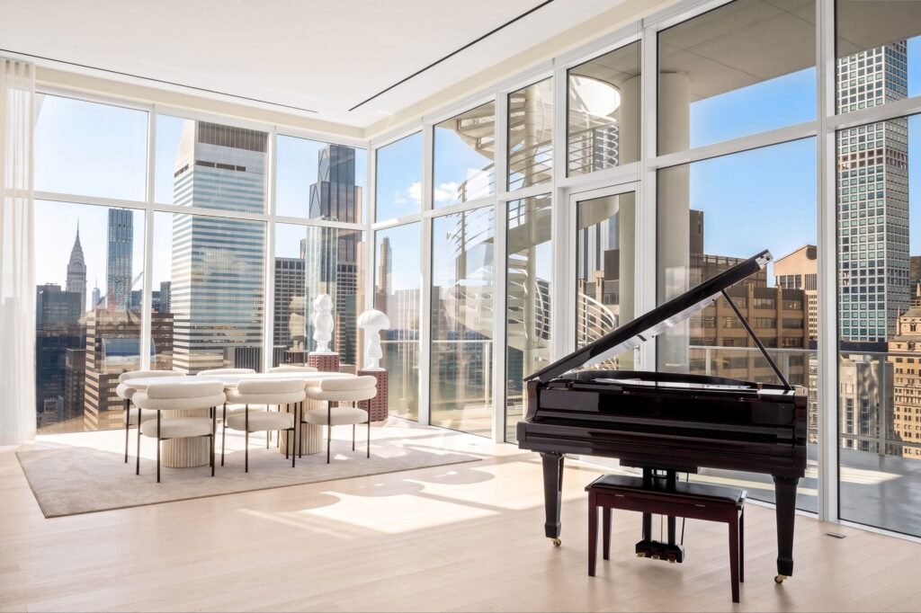 A black grand piano and modern dining set inside the luxury penthouse at The Elysia (200 East 59th Street) featuring floor-to-ceiling windows with panoramic views of the Manhattan skyline.